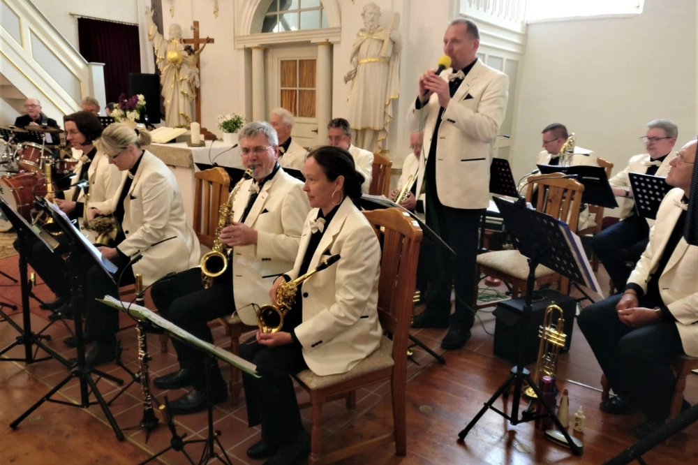 Kirchenkonzert Thüringen. Blaskapelle in weißen Jackets mit Sänger/Moderator – festliche Blasmusik-Impressionen.